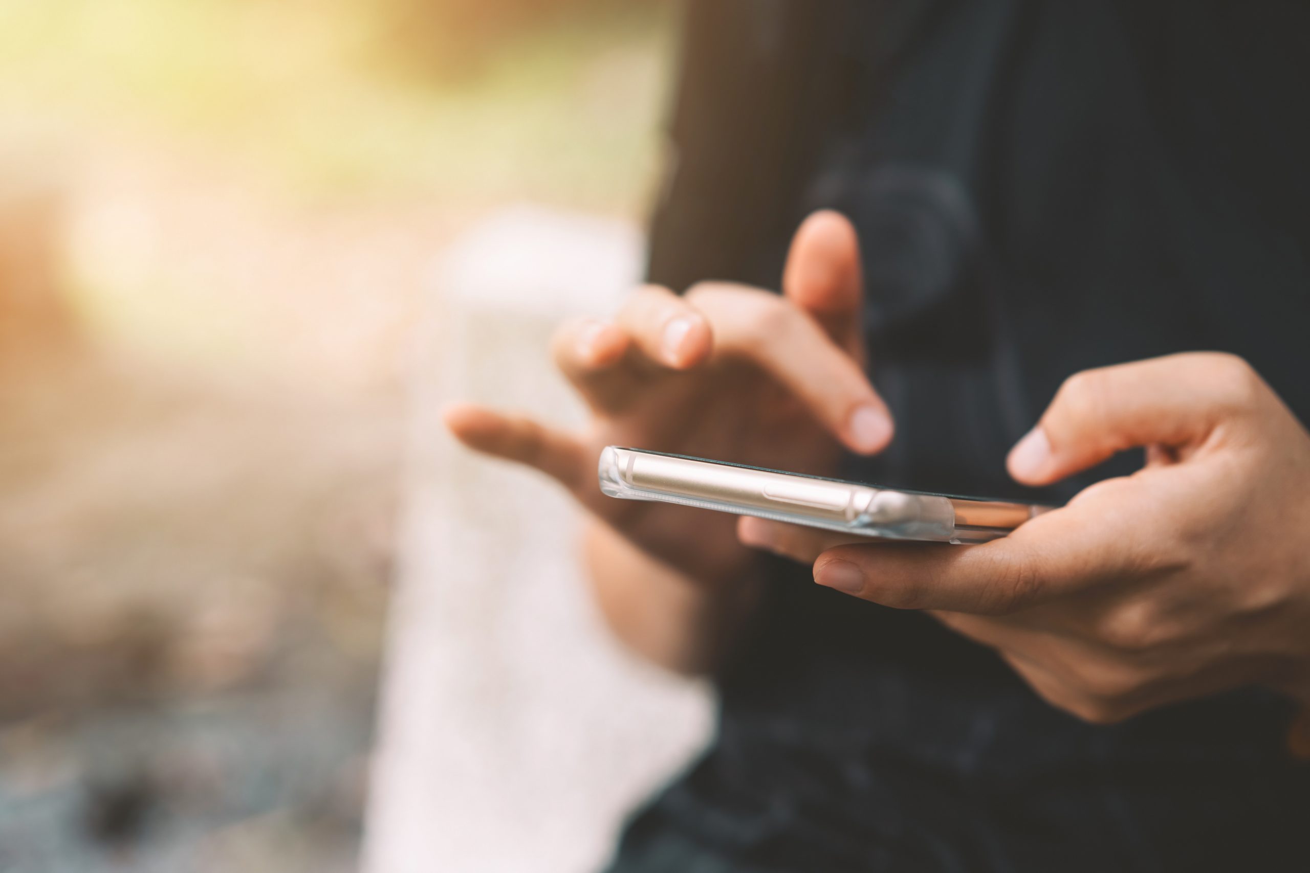 Närbild på en persons hand som håller en telefon i en utomhus miljö.